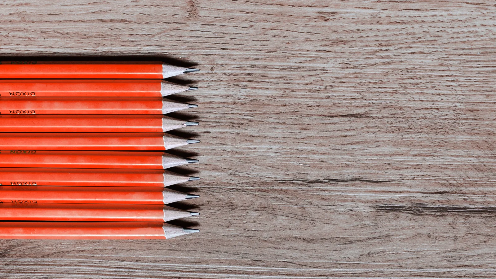 A row of red pencils on a wooden desk